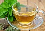 Close-up of a glass cup of lemon balm tea with fresh lemon balm leaves on top, set on a wooden table with natural sunlight.