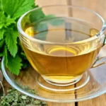 Close-up of a glass cup of lemon balm tea with fresh lemon balm leaves on top, set on a wooden table with natural sunlight.