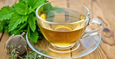 Close-up of a glass cup of lemon balm tea with fresh lemon balm leaves on top, set on a wooden table with natural sunlight.