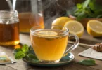 Close-up of a steaming glass of medicine ball tea with lemon and mint, highlighting its warm golden color.