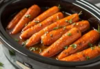 Carrots cooked with maple and brown sugar in a slow cooker, garnished with herbs.